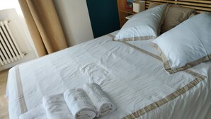 A neatly made bed with white linens and beige accents, a stack of folded towels, and a wooden headboard.