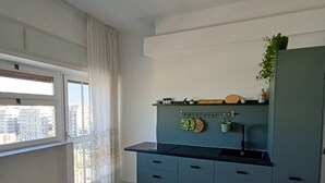 A modern kitchen with a marble floor, a window with curtains, and a view of buildings outside.