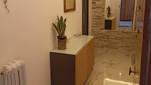A modern bathroom with a marble floor, a wooden vanity, a potted plant, and a framed botanical print on the wall.