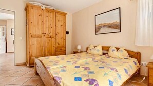 Ein Schlafzimmer mit einem Holzschrank, einem Bett mit floralem Bettzeug, einem Nachttisch und einem an der Wand hängenden Bild.