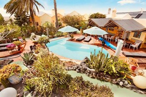 Ein Poolbereich mit Liegestühlen und Sonnenschirmen, umgeben von Pflanzen und einem kleinen Wasserfall.