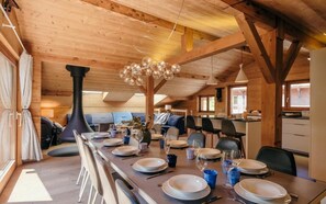 Interior de madera con una mesa de comedor dispuesta para seis personas, una lámpara negra grande y una estructura de techo de madera.