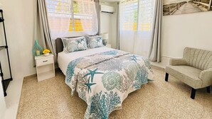 A bedroom with a bed, nightstand, chair, and a wall with a picture.