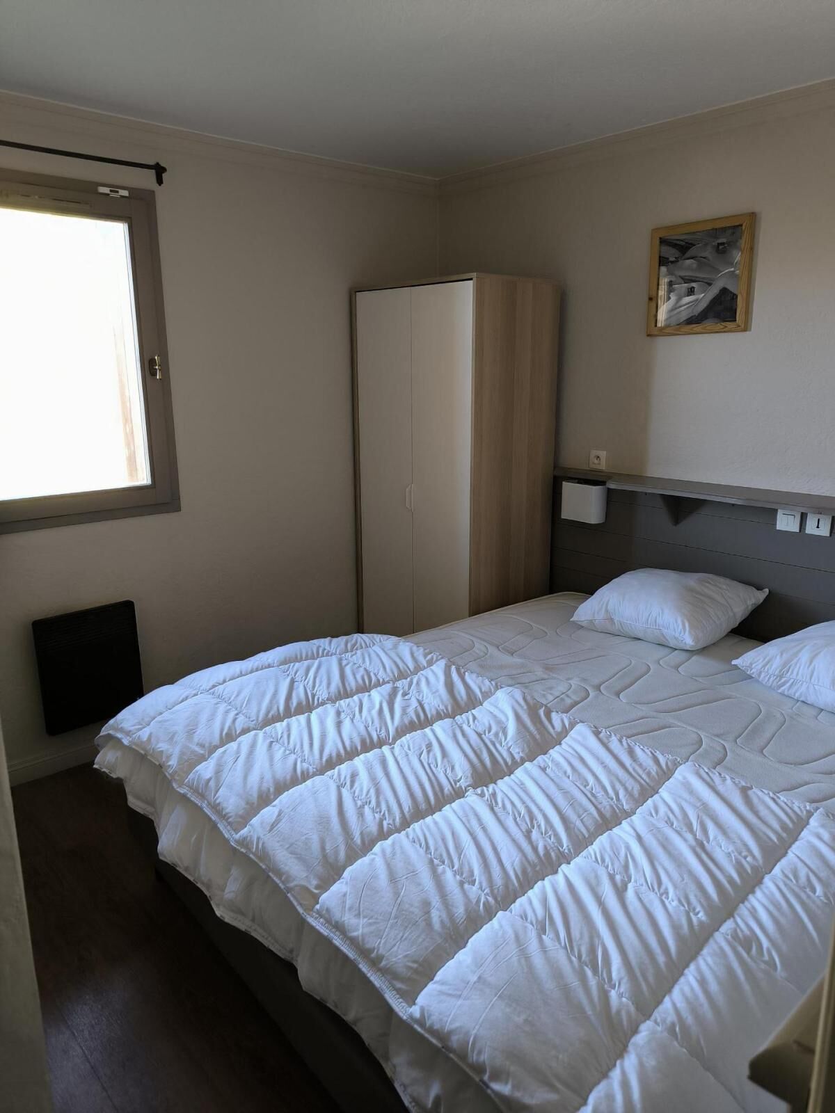 A bedroom with a bed, a wardrobe, a radiator, and a window.