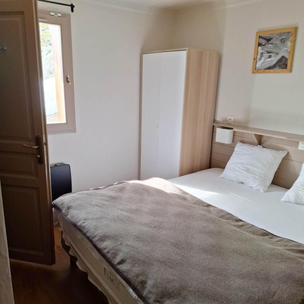 A bedroom with a bed, a wardrobe, a bedside table, and a window.