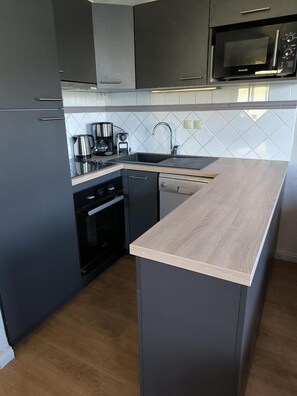 A modern kitchen with grey cabinetry, a wooden countertop island, a built-in oven, and a microwave above the sink.
