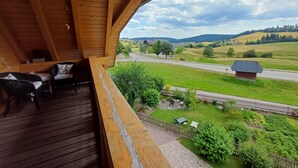 A wooden balcony with a view of a rural landscape, including a road and fields.