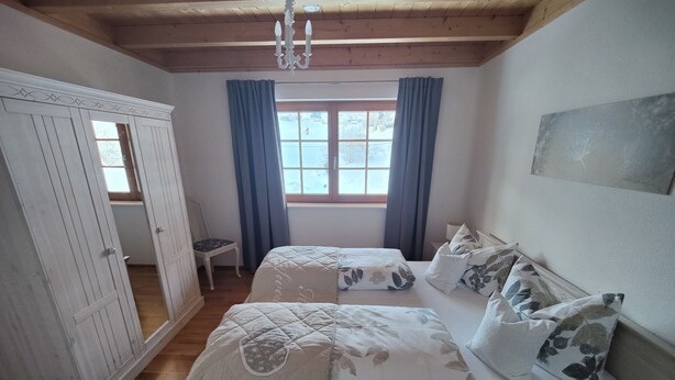 A bedroom with a bed, a wardrobe, a window with curtains, and a chandelier.