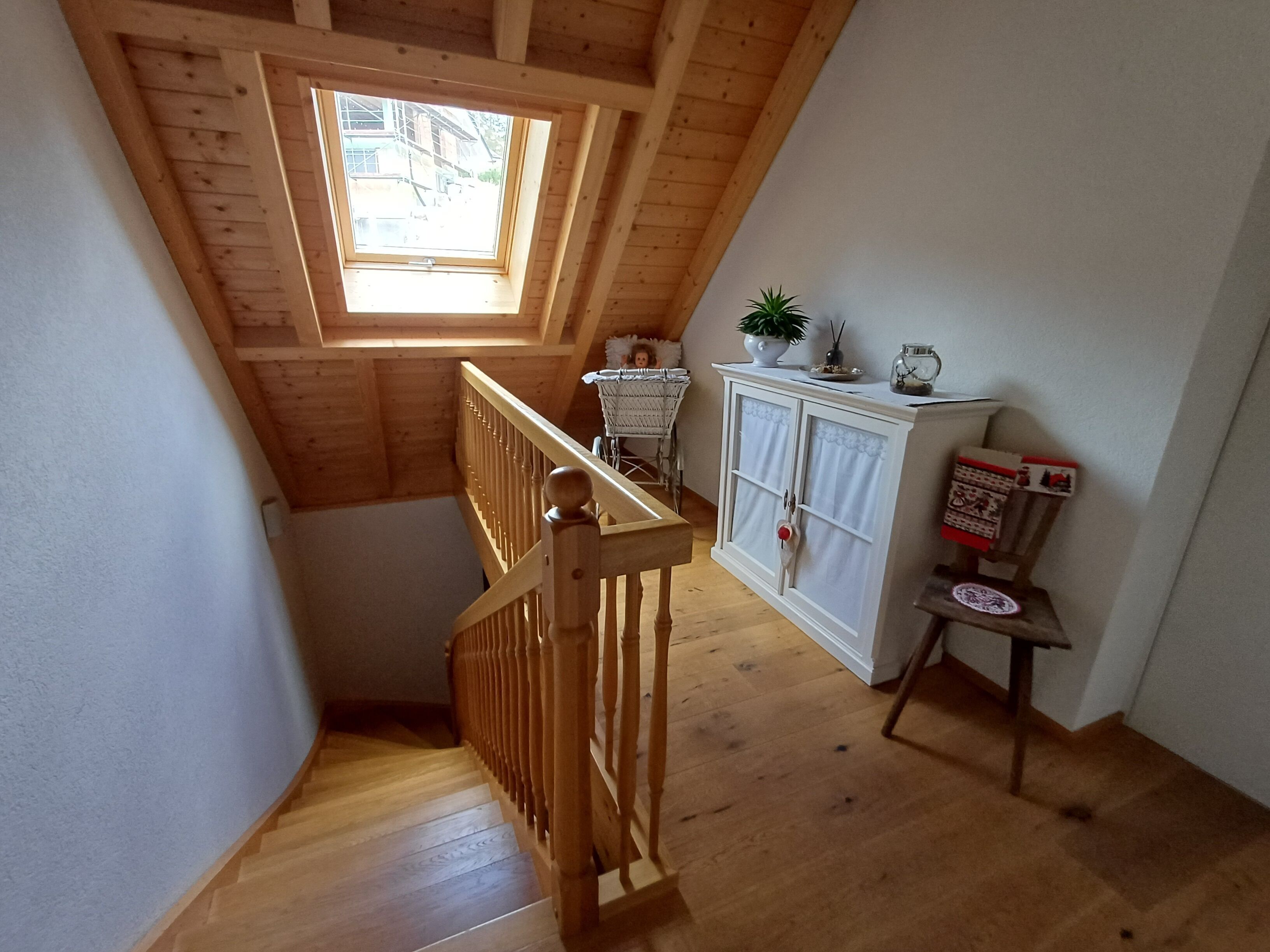 Un escalier en bois avec une lucarne donnant sur un espace aménagé en mezzanine.