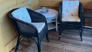 A wooden deck with two wicker chairs and a small table, featuring a simple, rustic design.