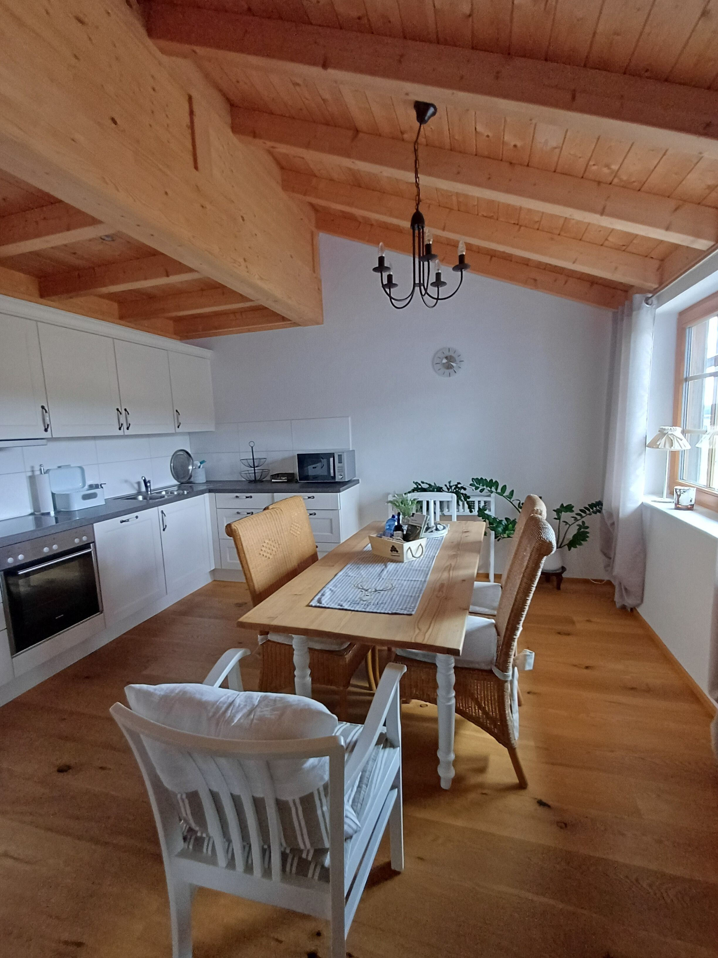 Une cuisine avec des meubles blancs, un four à micro-ondes et un coin repas comprenant une table et des chaises en bois.