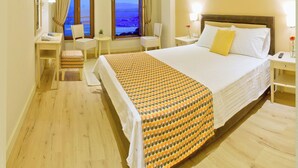 A hotel room with a large bed, a desk, a chair, and a view of the sea through two windows. - Arktos hotel (Ioannina)