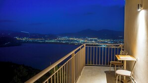 A balcony with a table and chairs, overlooking a cityscape at night. - Arktos hotel (Ioannina)