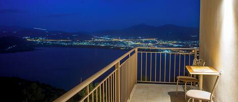 A balcony with a table and chairs, overlooking a cityscape at night.