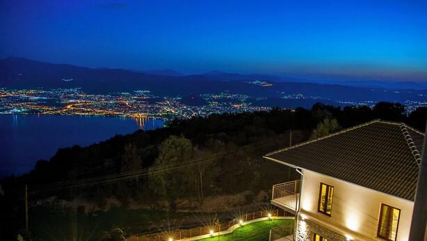 A two-story house with a stone facade, a balcony, and a view of a cityscape at night. - Arktos hotel (Ioannina)