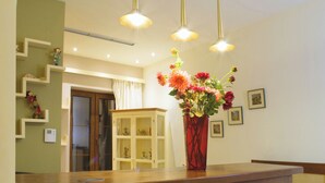 A dining area with a wooden table, a vase of flowers, pendant lights, and a staircase with shelves. - Arktos hotel (Ioannina)