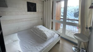 A bedroom with a bed, a window with a view of a snowy landscape, and a wooden wall. - 200m from ski slopes, 5th floor, balcony, tv, 43m², Les Arcs (Les Arcs)