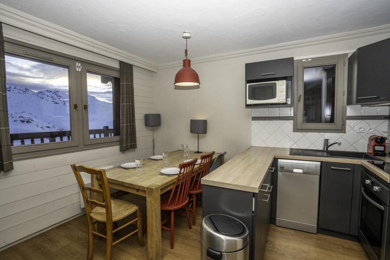 Una cocina moderna con una mesa de comedor de madera, sillas rojas, microondas integrado y lavavajillas.
