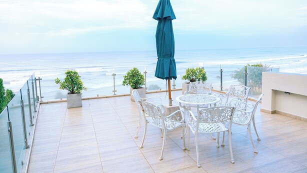 A terrace with a table and chairs, a blue umbrella, and a view of the ocean. - Surendra Seaview (Matara)