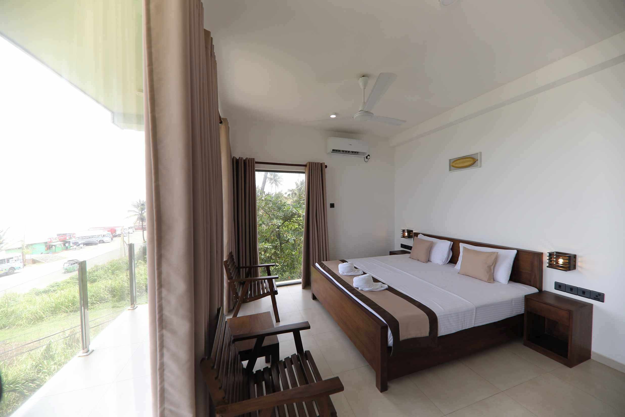A hotel room with a large bed, a desk, and a balcony with a view of the street.