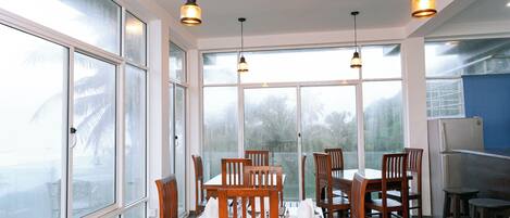 A dining area with large windows, wooden chairs, and hanging pendant lights.
