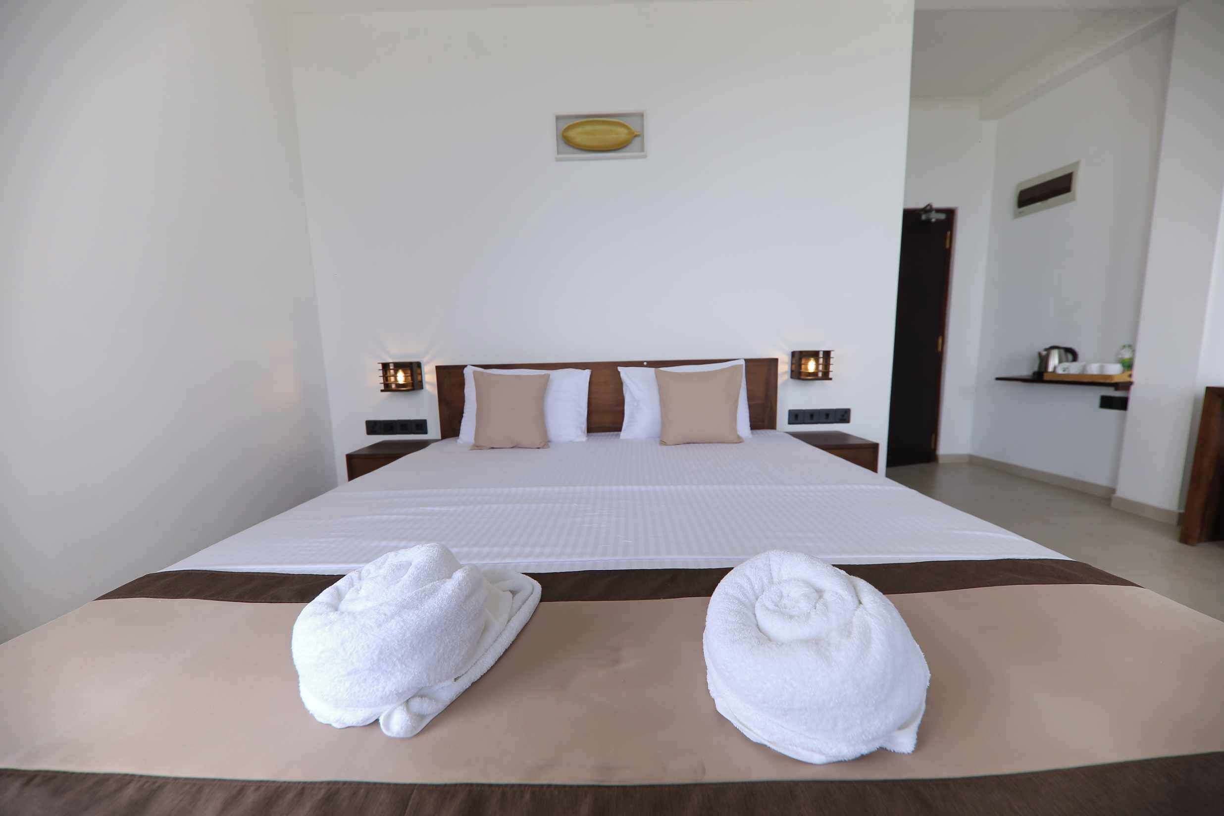 Een hotelkamer met een groot bed, twee nachtkastjes en een klein plankje met een waterkoker.