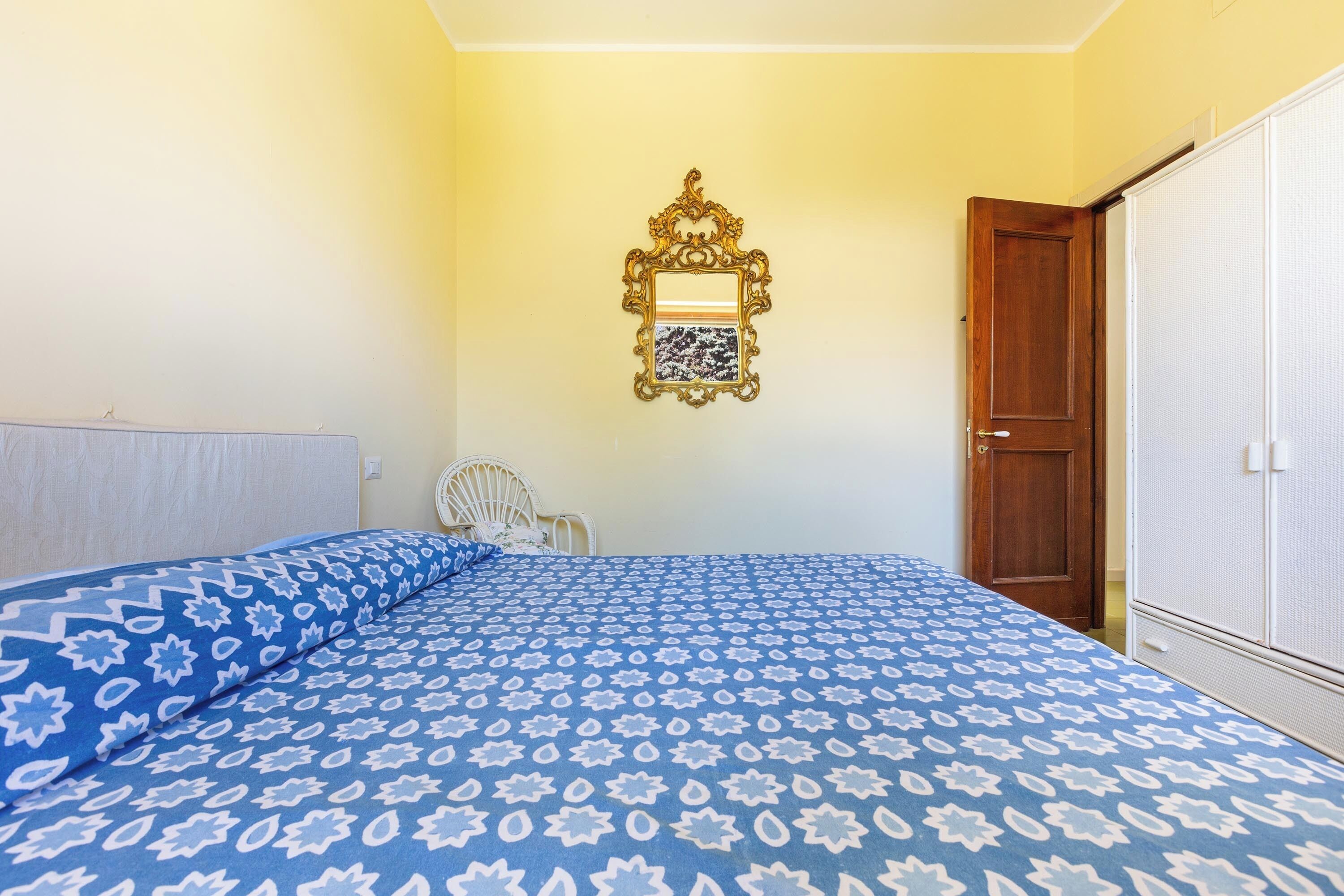 A bedroom with a bed, a chair, a wardrobe, and a door.