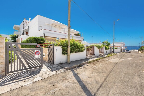 A modern white building with a gated entrance, a clear blue sky, and a view of the sea in the distance. - Terrazze sullo Ionio by BarbarHouse (Santa Caterina)