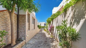 Une ruelle étroite pavée de pierres, bordée de bâtiments aux façades en briques et en stuc, et agrémentée d’une végétation luxuriante.