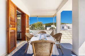 A balcony with a table set for two, wicker chairs, and a view of the surrounding landscape. - Terrazze sullo Ionio by BarbarHouse (Santa Caterina)