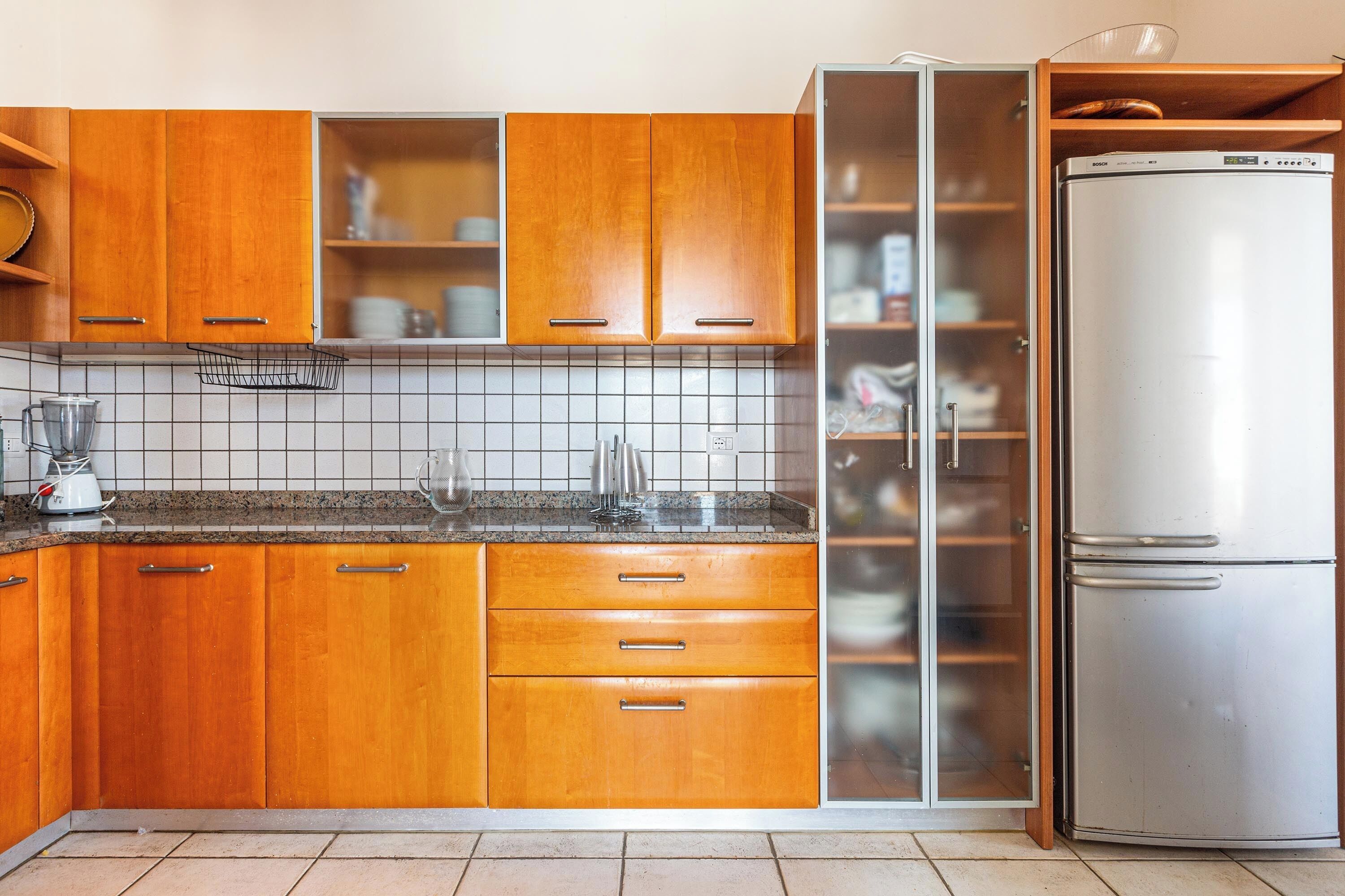 A kitchen with wooden cabinets, a stainless steel refrigerator, and a tiled backsplash.