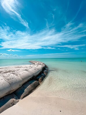 A beach with clear turquoise water, a sandy shore, and a large, curved concrete structure. - Whyknot Holbox (Isla Holbox)