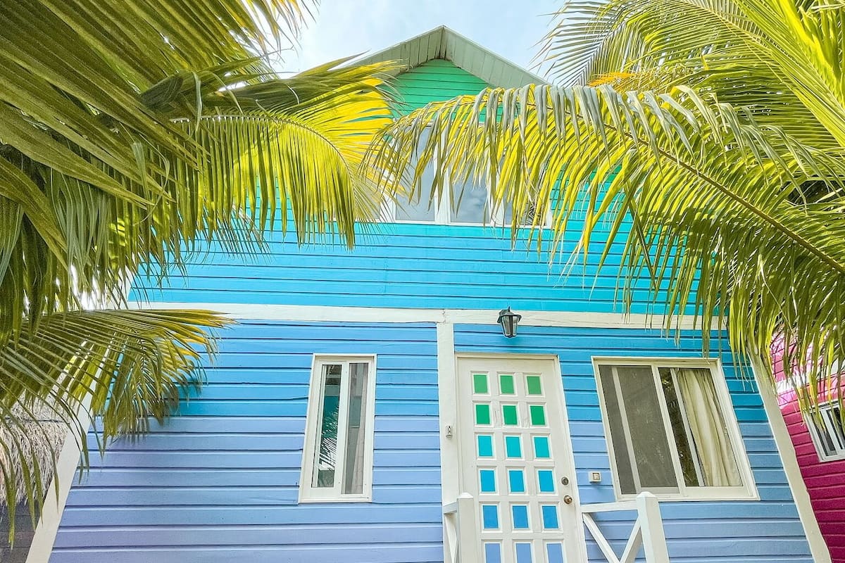 Uma casa de dois andares com fachada azul, uma porta branca e uma janela pequena.