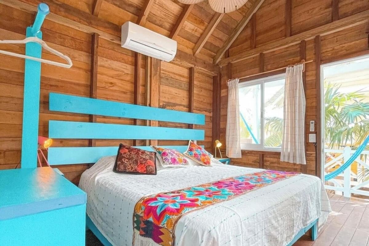 Quarto de cabana de madeira com cama, ventilador de teto e aparelho de ar condicionado.