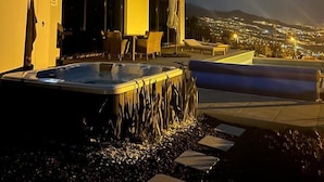 Zona de piscina exterior moderna amb banyera d'hidromassatge, gandules i una vista a la ciutat al capvespre.