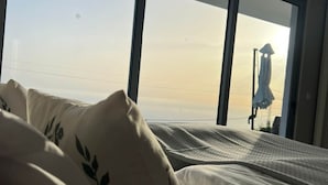 Habitació d'hotel amb una finestra gran, un llit amb almofadines florals i vista al cel.