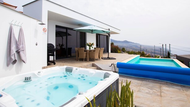 Zona de piscina exterior moderna amb una banyera d'hidromassatge, joc de menjador i vista a la ciutat.
