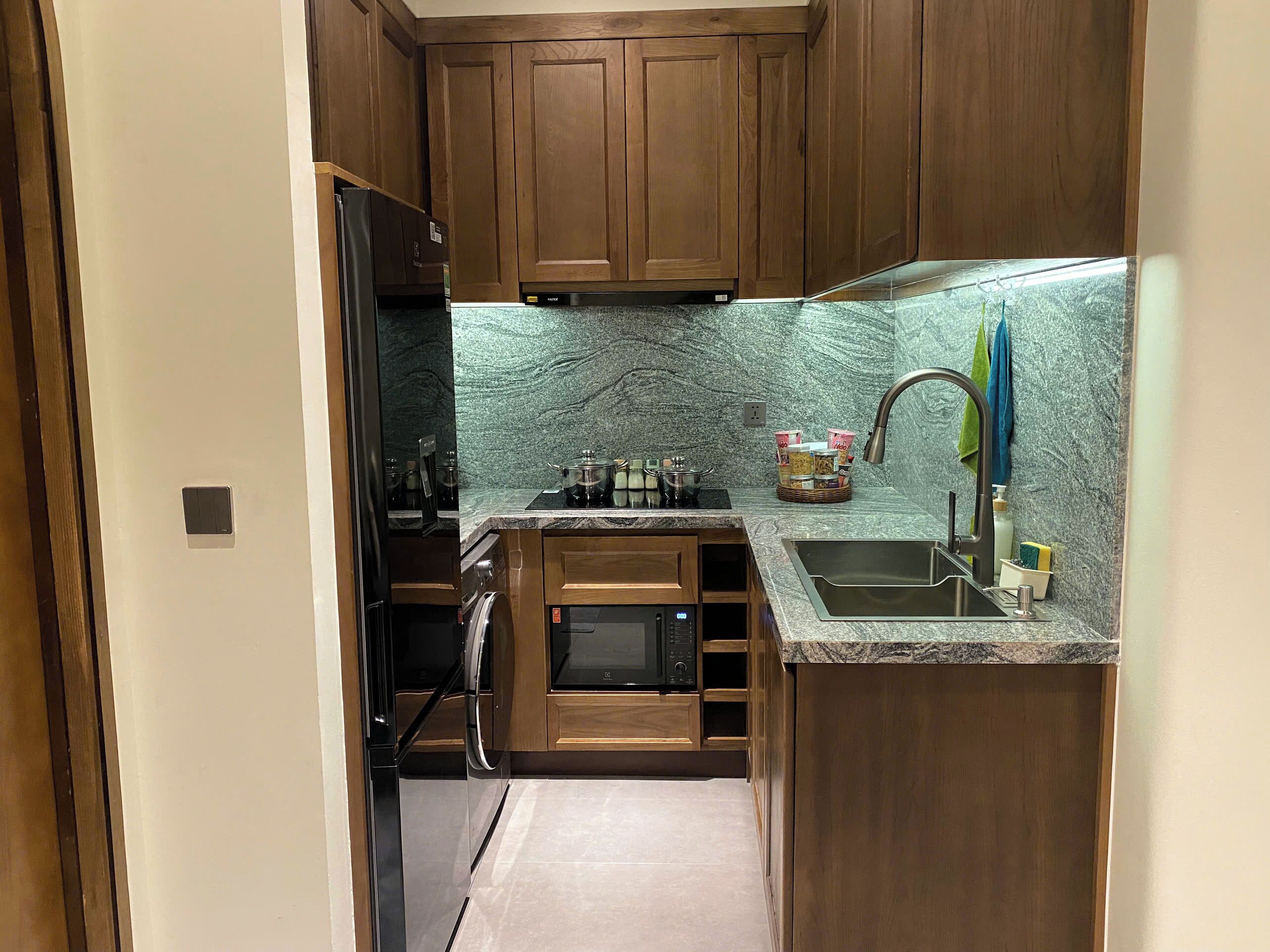Una cocina compacta con armarios de madera, microondas integrado, pileta de acero inoxidable y encimera de granito.