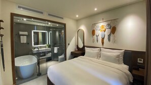 A modern hotel room with a large bed, a glass-enclosed shower, a vanity with a mirror, and a wall-mounted artwork. - JB Serviced Apartment Phu Quoc (Phu Quoc)