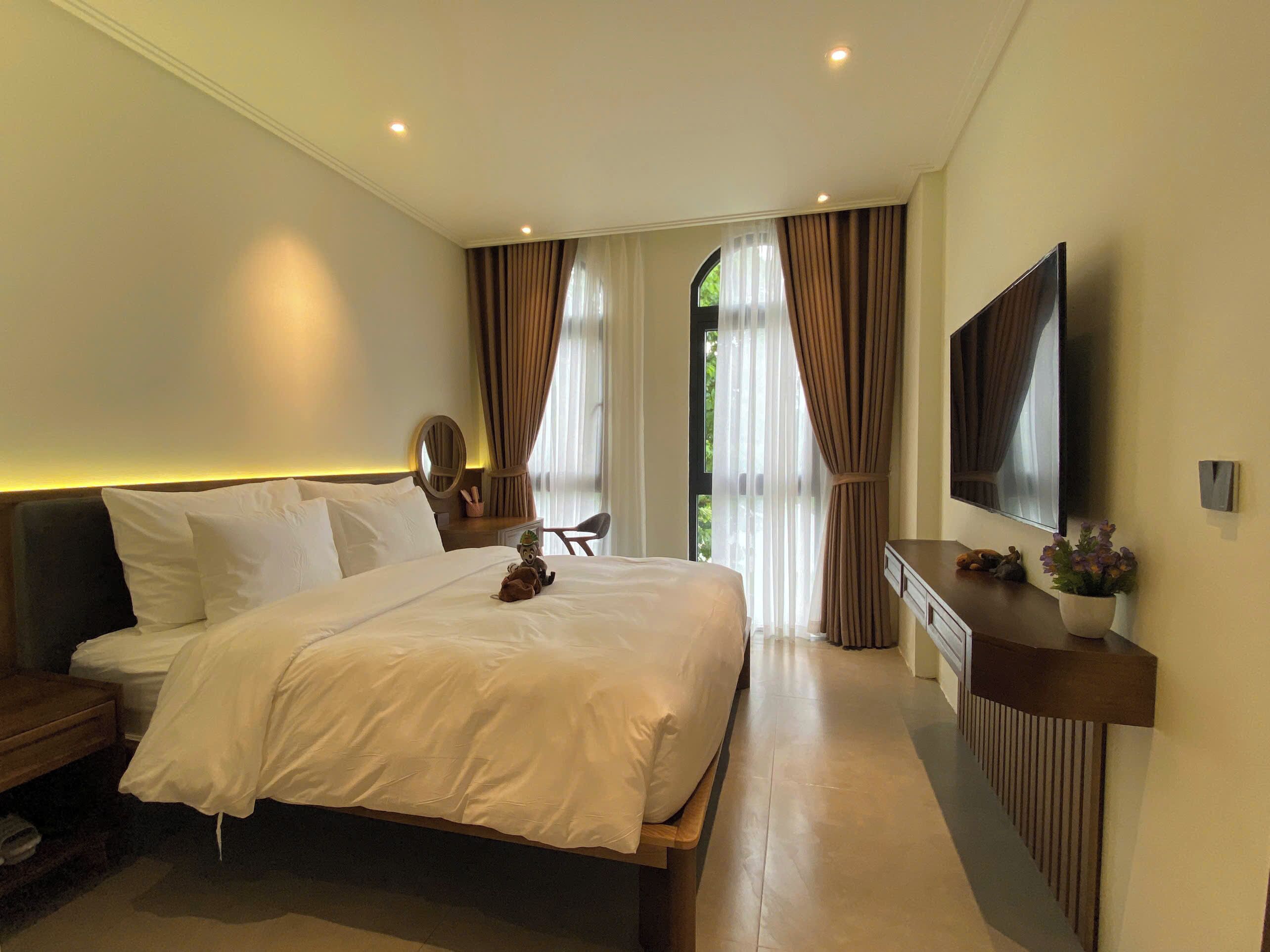 Quarto de hotel moderno com uma cama grande, uma mesa de trabalho, uma televisão e vista para o exterior.