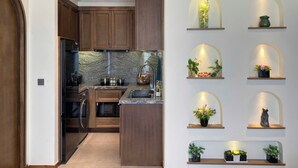 A modern kitchen with wooden cabinets, a built-in oven, and a granite countertop. There are multiple shelves with plants and decorative items. - JB Serviced Apartment Phu Quoc (Phu Quoc)