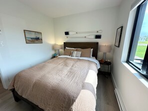 A hotel room with a large bed, two bedside tables with lamps, a painting on the wall, and a window with a view.