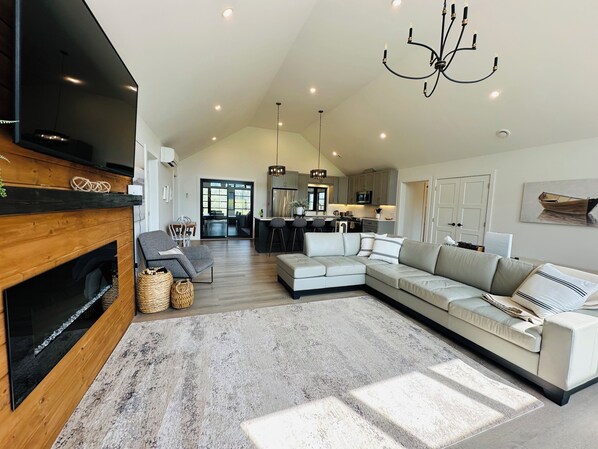 A spacious living area with a fireplace, a large sectional sofa, and a modern kitchen in the background.