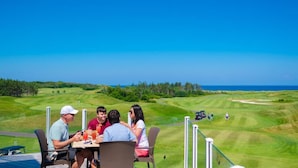 Un grupo de personas cenando en una mesa con vista a un campo de golf y al océano.