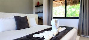 Una cama bien hecha con una toalla doblada, una almohada y una ventana con vistas a la vegetación.