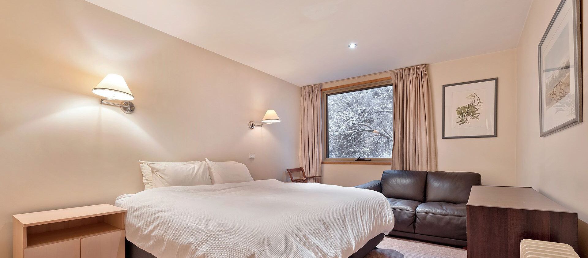 A bedroom with a bed, bedside tables, a chair, a desk, a window with curtains, and framed botanical prints on the wall.