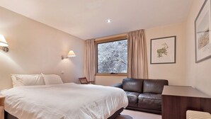 A bedroom with a bed, bedside tables, a chair, a desk, a window with curtains, and framed botanical prints on the wall.