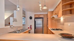 A modern kitchen with a double sink, stainless steel appliances, wooden cabinets, and pendant lighting.