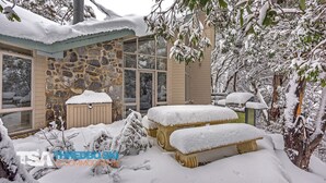 A stone building with large windows, a covered outdoor seating area, and snow-covered trees.