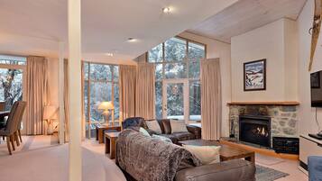 A cozy living room with a fireplace, large windows, and a dining area.